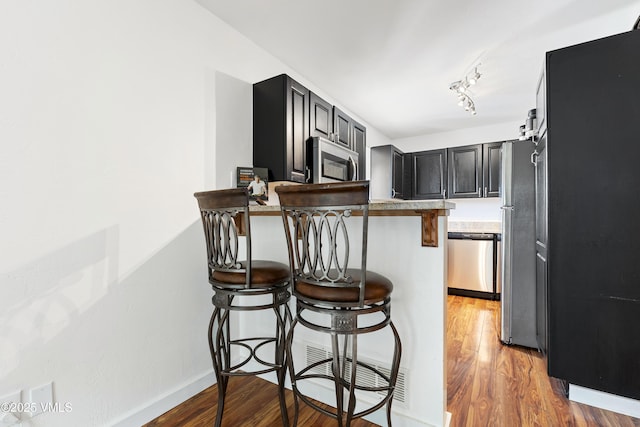 kitchen featuring stainless steel appliances, a peninsula, light wood-style floors, light countertops, and a kitchen bar