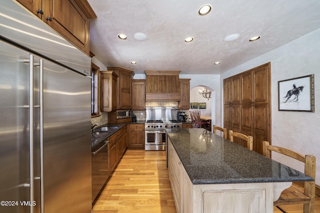 kitchen with dark stone countertops, a center island, built in appliances, a kitchen bar, and light wood-type flooring