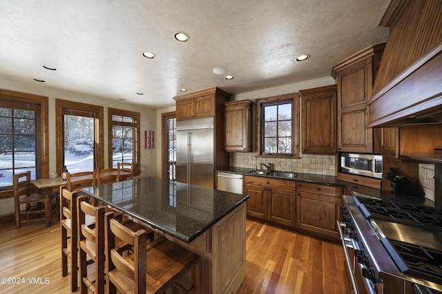 kitchen featuring sink, a center island, high end appliances, custom range hood, and light wood-type flooring