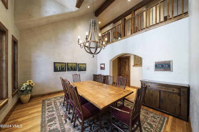 dining space with light wood-type flooring, a chandelier, beam ceiling, and a towering ceiling