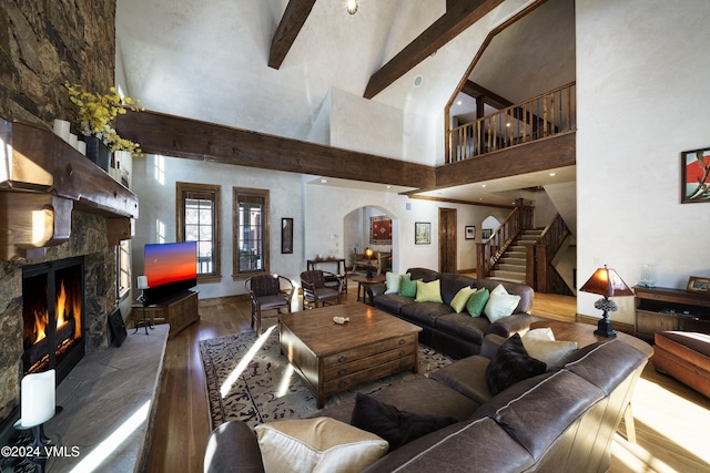 living room with hardwood / wood-style flooring, a towering ceiling, a high end fireplace, and beamed ceiling