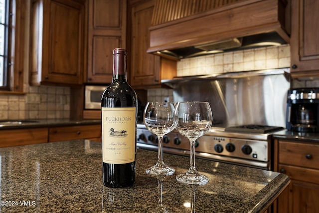 kitchen featuring tasteful backsplash, range, custom exhaust hood, and dark stone countertops