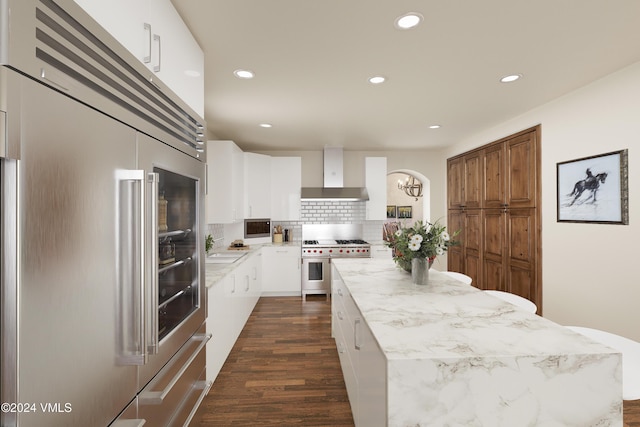 kitchen featuring wall chimney range hood, white cabinetry, a center island, high quality appliances, and tasteful backsplash