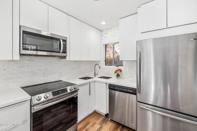 kitchen with sink, appliances with stainless steel finishes, white cabinetry, backsplash, and light hardwood / wood-style floors