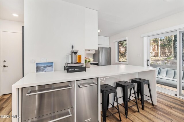 kitchen featuring a kitchen bar, appliances with stainless steel finishes, kitchen peninsula, light hardwood / wood-style floors, and white cabinets