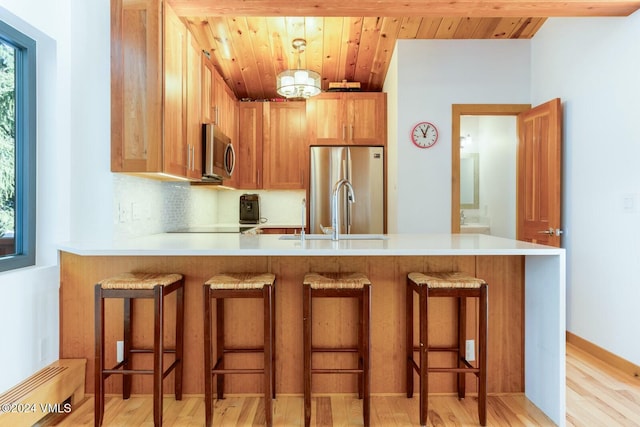 kitchen featuring stainless steel appliances, a kitchen breakfast bar, tasteful backsplash, wooden ceiling, and kitchen peninsula