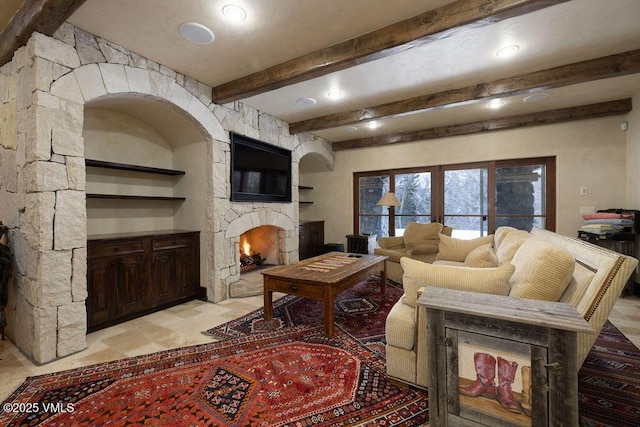 living area featuring beamed ceiling, built in shelves, a fireplace, and stone finish flooring