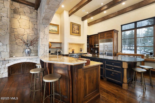 kitchen featuring dark wood-type flooring, a kitchen breakfast bar, light stone counters, and built in refrigerator