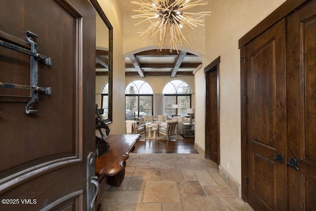 entrance foyer with beamed ceiling, a notable chandelier, coffered ceiling, stone tile flooring, and arched walkways