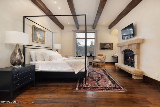 bedroom featuring baseboards, wood-type flooring, beam ceiling, and a fireplace