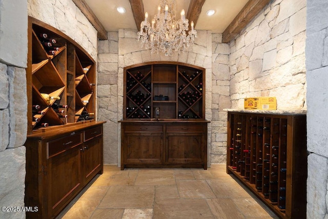 wine area with recessed lighting, a chandelier, beam ceiling, and stone tile flooring