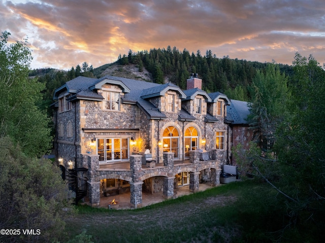 8 Rue Riviere Rd, Edwards, CO 81632 - back of property at dusk with stone siding, a chimney, a patio area, and a forest view