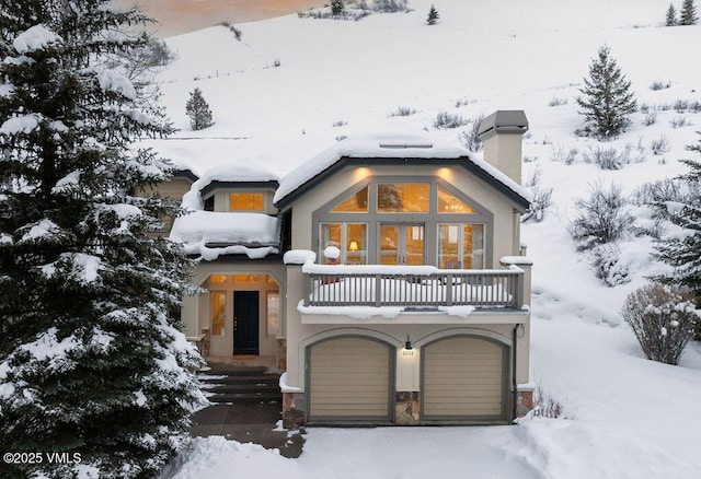 view of front of house featuring a chimney, an attached garage, and a balcony