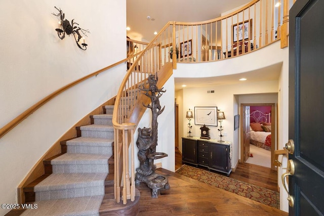 staircase featuring recessed lighting, a high ceiling, visible vents, and wood finished floors