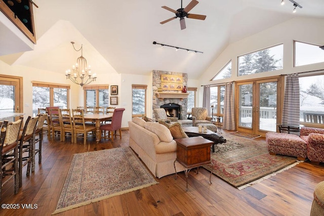 living room featuring hardwood / wood-style floors, a stone fireplace, high vaulted ceiling, rail lighting, and ceiling fan with notable chandelier
