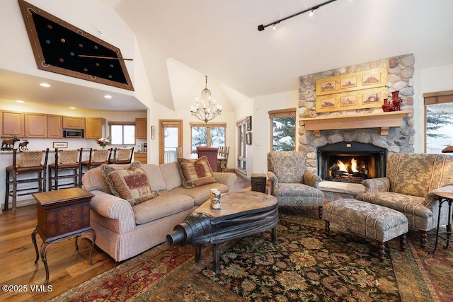 living area featuring a notable chandelier, light wood finished floors, a fireplace, high vaulted ceiling, and rail lighting