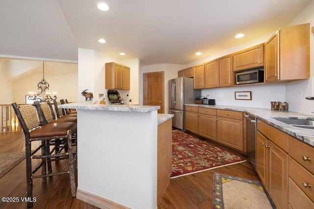 kitchen featuring dark wood-style flooring, a breakfast bar, a sink, appliances with stainless steel finishes, and a notable chandelier