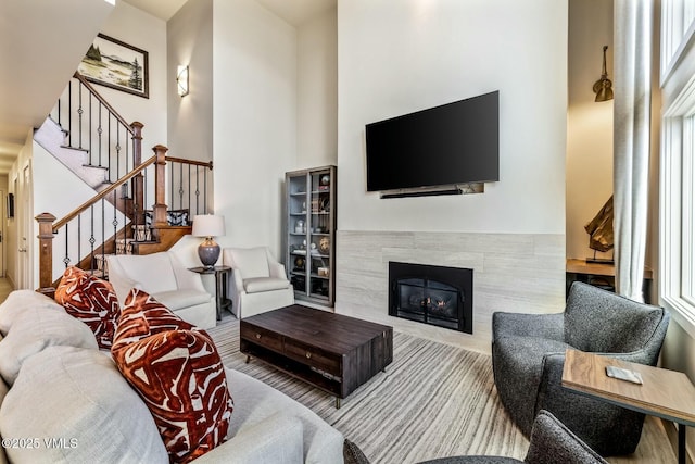 living room featuring a tile fireplace, a high ceiling, and stairs