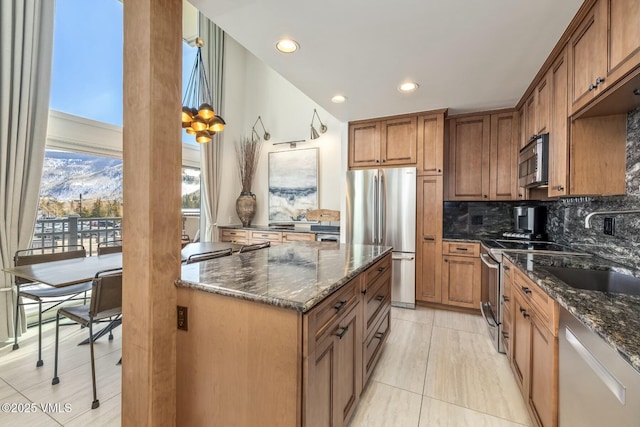 kitchen featuring backsplash, appliances with stainless steel finishes, brown cabinetry, a sink, and dark stone counters