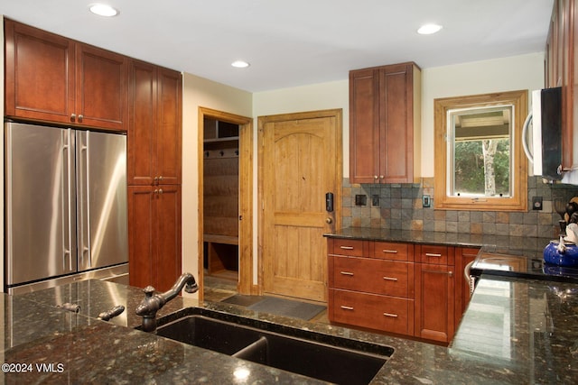 kitchen with stainless steel appliances, tasteful backsplash, sink, and dark stone countertops