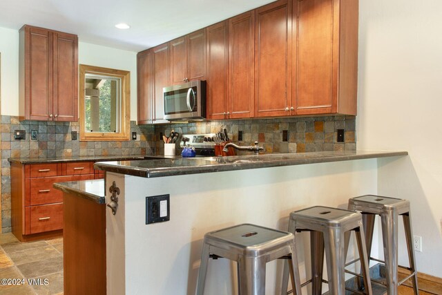 kitchen featuring tasteful backsplash, a breakfast bar area, kitchen peninsula, and dark stone counters