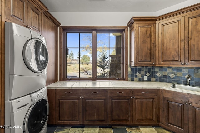 laundry room with cabinets, stacked washer and clothes dryer, and sink