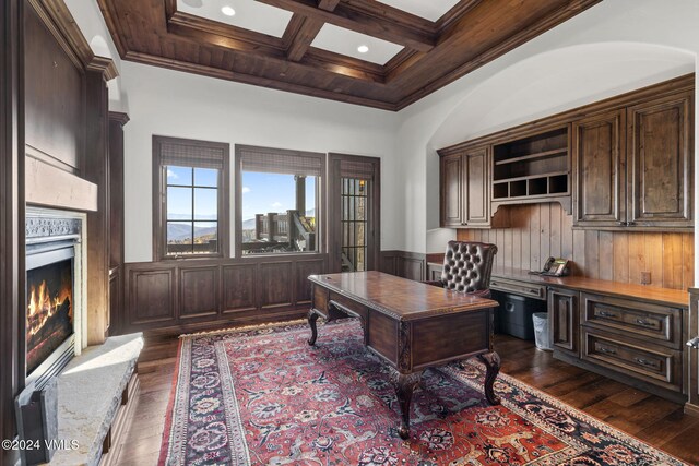 office area featuring dark wood-type flooring, a towering ceiling, coffered ceiling, a high end fireplace, and ornamental molding