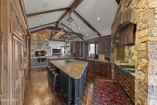 kitchen with dark stone countertops, a center island, lofted ceiling with beams, dark hardwood / wood-style flooring, and stainless steel gas stovetop