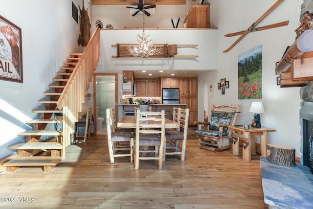 dining room with a towering ceiling, ceiling fan with notable chandelier, and light hardwood / wood-style floors