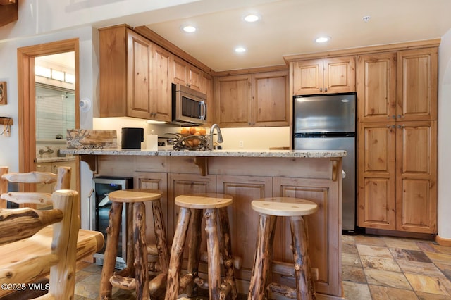 kitchen with a breakfast bar, light brown cabinetry, kitchen peninsula, stainless steel appliances, and light stone countertops