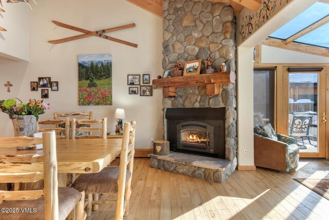 dining space with beam ceiling, high vaulted ceiling, a stone fireplace, and light hardwood / wood-style floors