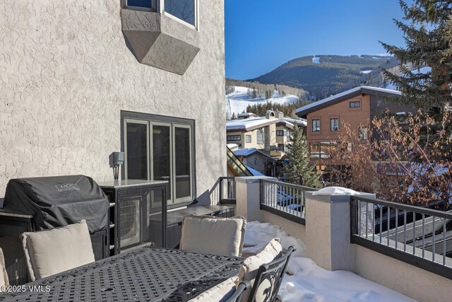 snow covered patio with a mountain view, a balcony, and a grill