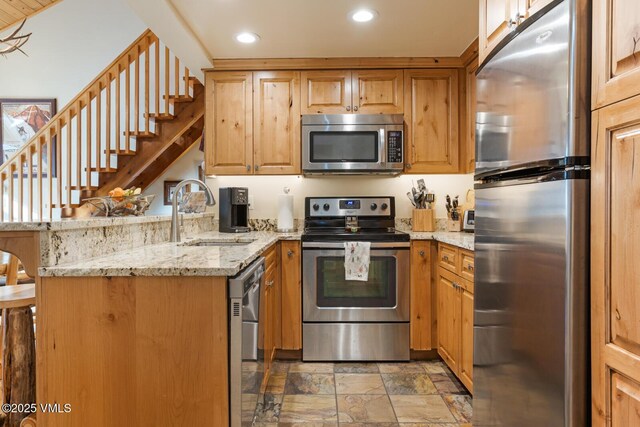 kitchen featuring appliances with stainless steel finishes, sink, a breakfast bar area, kitchen peninsula, and light stone countertops