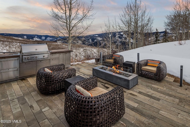 snow covered patio with an outdoor kitchen, grilling area, a mountain view, and a fire pit