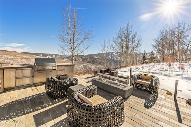 snow covered deck with grilling area, exterior kitchen, a patio, and a mountain view