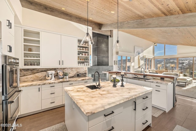 kitchen with sink, light stone counters, white cabinetry, hanging light fixtures, and an island with sink