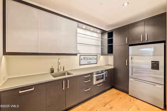 kitchen with appliances with stainless steel finishes, sink, and light hardwood / wood-style flooring