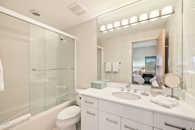 full bathroom featuring vanity, bath / shower combo with glass door, tile walls, and toilet