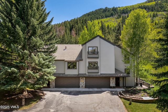 130 Grouse Ct Unit B, Avon, CO 81620 - view of front of home with a balcony, a view of trees, driveway, a garage, and stone siding