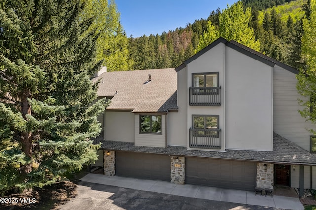 130 Grouse Ct Unit B, Avon, CO 81620 - view of front of property with stone siding, a forest view, a shingled roof, driveway, and a garage
