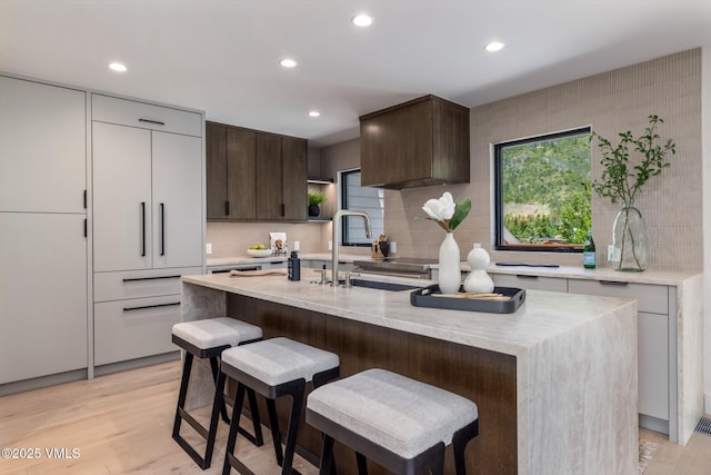 5074 Main Gore Dr S Unit B, Vail, CO 81657 - kitchen featuring decorative backsplash, dark brown cabinetry, light wood finished floors, a breakfast bar area, and an island with sink