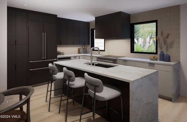 kitchen featuring sink, paneled built in refrigerator, light hardwood / wood-style floors, a center island with sink, and decorative backsplash