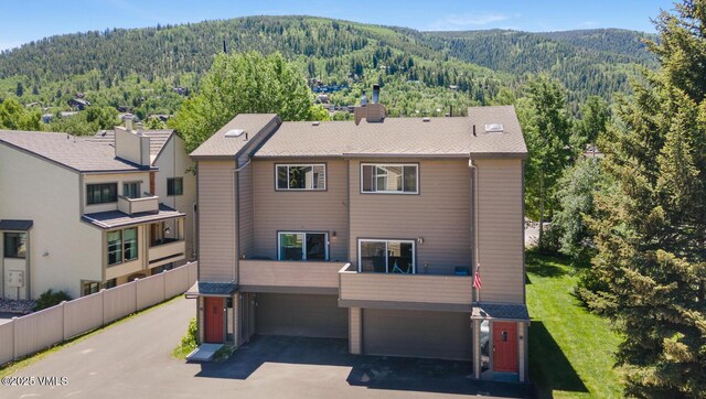 89 Columbine Cir Unit 2, Avon, CO 81620 - back of property with a wooded view, a mountain view, an attached garage, asphalt driveway, and a chimney