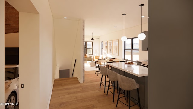 kitchen featuring hanging light fixtures, ceiling fan, a kitchen breakfast bar, and light hardwood / wood-style floors