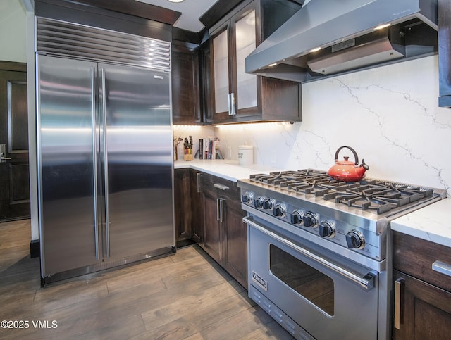 320 Hummingbird Dr Unit A201, Avon, CO 81620 - kitchen featuring premium appliances, wall chimney range hood, dark brown cabinets, and glass insert cabinets