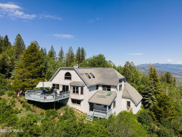 back of house with a deck with mountain view and roof with shingles