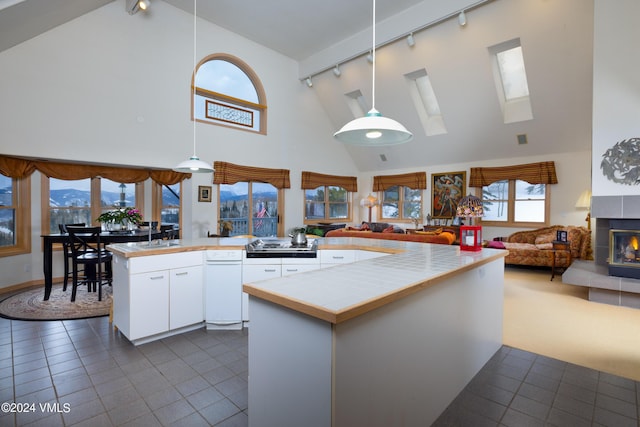 kitchen featuring tile counters, open floor plan, a tile fireplace, hanging light fixtures, and white cabinets