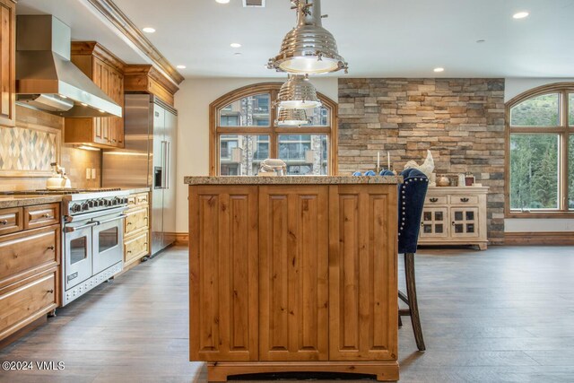 kitchen featuring wall chimney exhaust hood, premium appliances, a kitchen breakfast bar, dark hardwood / wood-style flooring, and pendant lighting