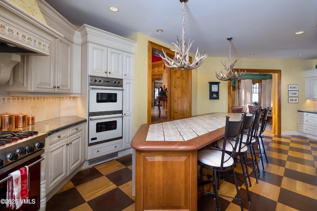 kitchen featuring a breakfast bar, decorative backsplash, stainless steel range, white cabinets, and white double oven