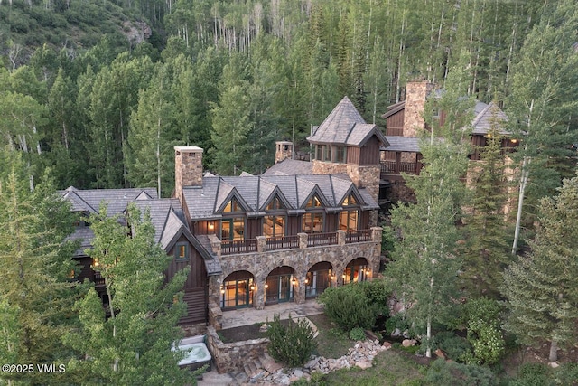 1094 Riva Gln, Vail, CO 81657 - rear view of house featuring a chimney, a wooded view, stone siding, a balcony, and board and batten siding
